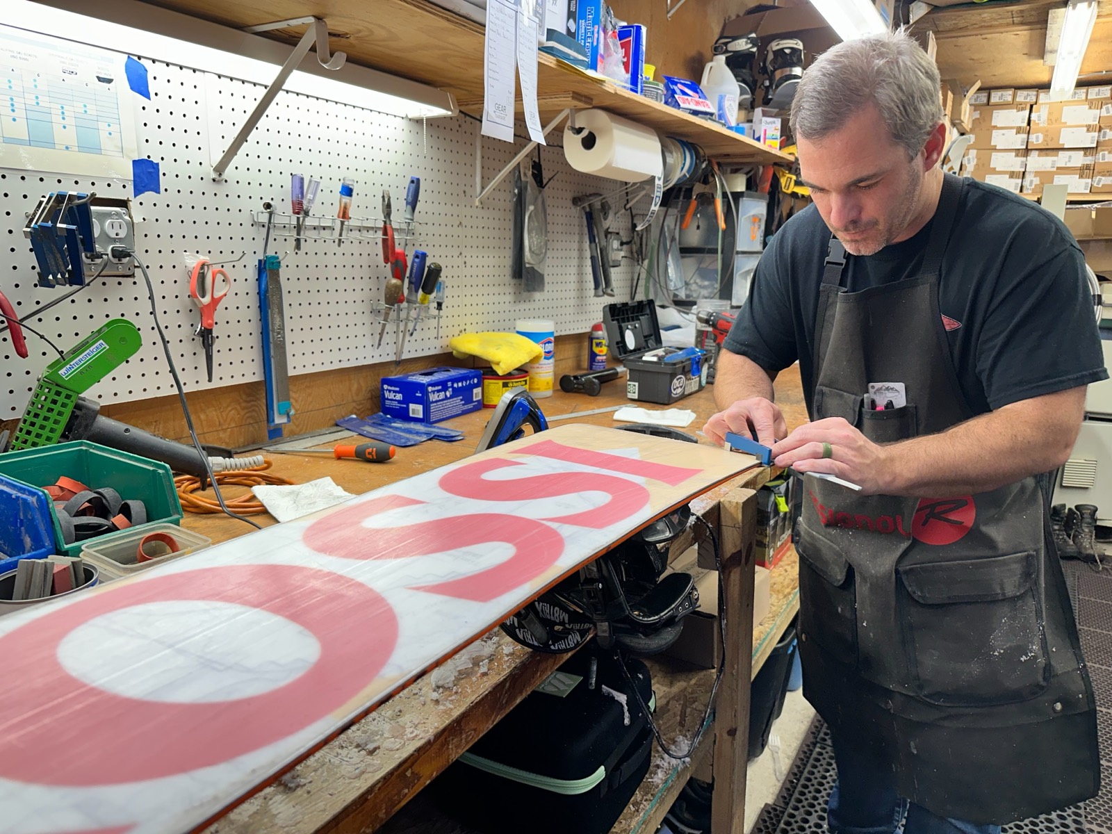 A Gear Garage tech sharpening the edge of a Rossignol snowboard at the tune bench